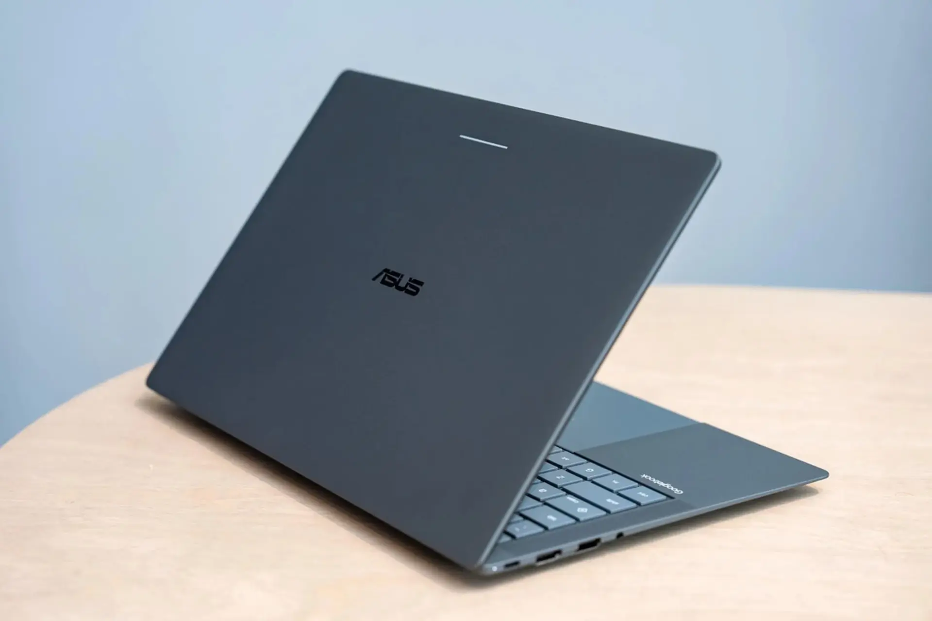 لپتاپ ایسوس (ASUS) با بدنه خاکستری روی میز چوبی